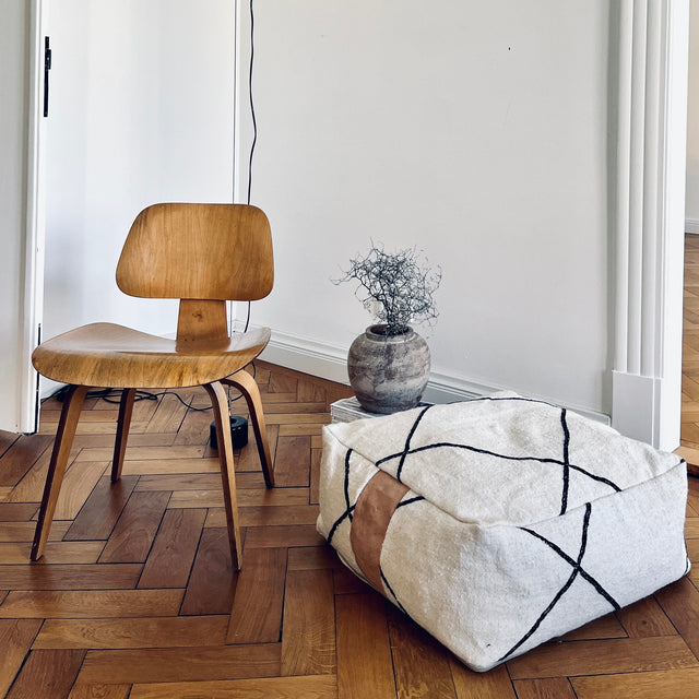 Bodenkissen in schwarz-weißem Kelim Design in Altbauwohnung auf Fischgrätparkett mit Holzstuhl und Designerlampe.