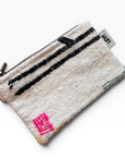 Die LEY! Tasche - Colorful Line (15 x 20) ist eine kleine gewebte Clutch mit Reißverschluss, weißem Boden, schwarzen Streifen, rosa geometrischem Muster in einer Ecke und einem seitlichen Stoffanhänger - ideal als multifunktionales Accessoire.