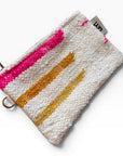 Die Tasche - Colorful Line - 15 x 20 von LEY! ist eine strukturierte weiße Reißverschlusstasche mit vertikalen rosa, orangen und gelben gewebten Streifen und einem kleinen Eckanhänger mit der Aufschrift "LEY!".