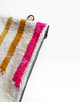 Nahaufnahme der Tasche - Colorful Line - 15 x 20 von LEY!: eine weiße, strukturierte Wolltasche mit gelben und rosafarbenen Diagonalstreifen, Metallreißverschluss und kleinem Metallring vor einem schlichten weißen Hintergrund.