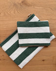 Zwei LEY! Tasche - Stripe Line "Tilosa" (20x30cm), handgefertigt mit grünen und weißen Streifen, eine kleine und eine große, beide mit Reißverschlüssen, abgebildet auf einer hellen Holzoberfläche.
