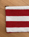 Die LEY! Tasche - Stripe Line "Symia" (20x30cm) besticht durch handgemachtes Streifendekor in Rot-Weiß und sichtbaren Reißverschluss an der linken Ecke - teils auf heller Holzfläche präsentiert.