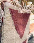Eine Person hält den Berber-Teppich „THE DANISH GIRL INTERIOR – Tazita“ (0,60 x 1,10 m) mit rosa Dreieck und Quasten in der Hand.