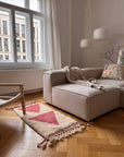 Ein beiges Sofa und der Berber-Teppich „Tazita“ von THE DANISH GIRL INTERIOR in einem sonnendurchfluteten Raum mit Holzböden und Pendelleuchten.