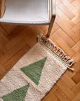 Beiger Stuhl von THE DANISH GIRL INTERIOR, Berber-Teppich – Noor, 0,60 × 1,10 m, mit grünen Dreiecken auf Holzboden.