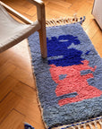 Berber-Teppich – Amani (0,60 x 1,10 m) von THE DANISH GIRL INTERIOR mit Quasten unter einem Stuhl auf einem Fischgrätenparkett.