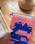 Der Berber-Teppich „Farah“ (0,60 x 1,10 m) von THE DANISH GIRL INTERIOR auf einem Holzboden, dazu ein Korb und ein Holzstuhl.