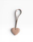 Der LEY! Taschenanhänger – Love Loop in Apricot verfügt über ein geschlungenes Band und wird auf weißem Hintergrund abgebildet.