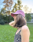 Eine Frau mit einer blauen LEY! „Habibi“-Kappe mit verstellbarem Verschluss lächelt auf dem Rasen, hinter ihr stehen Bäume.