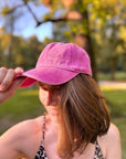 Jemand mit einer LEY!-Kappe in Lila steht draußen, hält den Schirm fest, im Hintergrund sind verschwommene Bäume zu sehen.