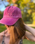 Eine Person trägt die LEY! „Yalla Yalla“-Kappe in Lila im Freien, im Hintergrund sind grüne Bäume schemenhaft zu erkennen.