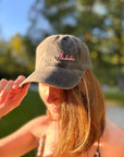 Eine Frau im Sonnenlicht trägt die LEY! „Habibi“-Kappe in Rosa mit verstellbarem Riemen, die die Krempe berührt; der Hintergrund ist unscharf.