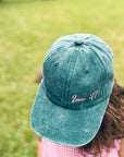 Person in einer „LEY!“-Kappe mit der Aufschrift „Love it“ in Grün von LEY!, im Vintage-Look, rosa Schriftzug, auf Gras, von oben gesehen.