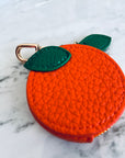 Orangefarbenes Schlüsselanhänger-Etui von LEY! mit grünen Details und Reißverschluss auf Marmortisch.