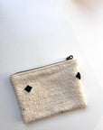 Eine kleine, handgefertigte, cremefarbene Tasche aus Schurwolle von LEY! mit Reißverschluss und zwei schwarzen Rautenmustern, die auf einer weißen Fläche ausgestellt sind.