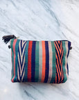 Eine lebendige, handgenähte TASCHE Tasche von LEY! mit einem Reißverschluss, vertikalen grünen, blauen, roten, orange-weißen Streifen und einer braunen Quaste liegt anmutig auf einer Marmoroberfläche.