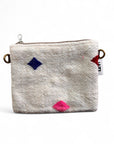Die LEY! Tasche - Colorful Line - 15x20cm ist eine kleine, strukturierte, cremefarbene Schurwolle-Tasche mit Metallringen, blau/rot/rosa Rautenmustern, einem weißen Seitenanhänger und handgefertigt im Stil der Handarbeit Marrakesch.