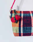 An der Wand hängt eine bunt karierte Mini-Etui-Kunstleder-Handtasche mit rosafarbenem Riemen, die mit dem LEY! Schlüsselanhänger - Kirsche und einem kleinen weißen Anhänger mit teilweise sichtbarer schwarzer Schrift.