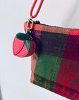 Eine Nahaufnahme eines lebhaft karierten Beutels mit einem rot-grün-schwarzen Karomuster. Der Reißverschluss ist mit dem Schlüsselanhänger - Pfirsich von LEY! verziert, was dieses Mini-Etui aus Kunstleder sowohl praktisch als auch stilvoll macht.