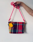 Eine Hand hält eine karierte Stoffhandtasche mit einem hellrosa Riemen und einem kleinen gelben LEY! Schlüsselanhänger - Zitrone angebracht, vor einem schlichten weißen Hintergrund.