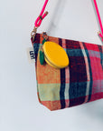 Eine leuchtend karierte Handtasche mit rosa Riemen, gelbem, rundem Münzbeutel und Mini Etui Kunstleder Schlüsselanhänger - Zitrone von LEY! mit weißem "LEY!"-Schriftzug wird vor einem schlichten weißen Hintergrund präsentiert.