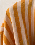 Eine Nahaufnahme des KIMONO - MEDITERANE - GELB - WEIß von THE DANISH GIRL INTERIOR zeigt vertikale gelbe und weiße Streifen, wobei die sanften Falten und die Textur des Stoffes vor einer schlichten hellen Wand sichtbar sind.