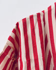 Eine Nahaufnahme des KIMONO - MEDITERANE - ROT - WEIß von THE DANISH GIRL INTERIOR zeigt den rot-weiß gestreiften Stoff, den geschwungenen Saum und einen Teil des Ärmels vor einem schlichten weißen Hintergrund.