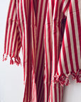 Eine Nahaufnahme des KIMONO - MEDITERANE - ROT - WEIß von THE DANISH GIRL INTERIOR zeigt den rot-weiß gestreiften, strukturierten, leichten Stoff mit ausgefransten Kanten - ideal für einen stilvollen Kimono-Bademantel oder Baumwollmantel.