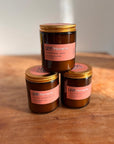 Drei braune Glasgefäße mit goldenen Deckeln und der Aufschrift "LEY! Moments" sind auf Holz gestapelt und enthalten jeweils LEY! Moments Duftkerze - Berber Soul (Sandelholz & Rose), einer Premium-Sojaduftkerze. Auf den rosafarbenen Etiketten sind die Duftdetails angegeben.