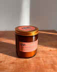 Eine braune Glaskerze mit goldenem Deckel der Marke LEY! steht auf einer Holzfläche im Sonnenlicht. Auf dem Etikett steht "LEY! Moments Duftkerze - Essouria Swell - Sea Salt", was darauf hinweist, dass es sich um eine hochwertige Sojawachskerze handelt.