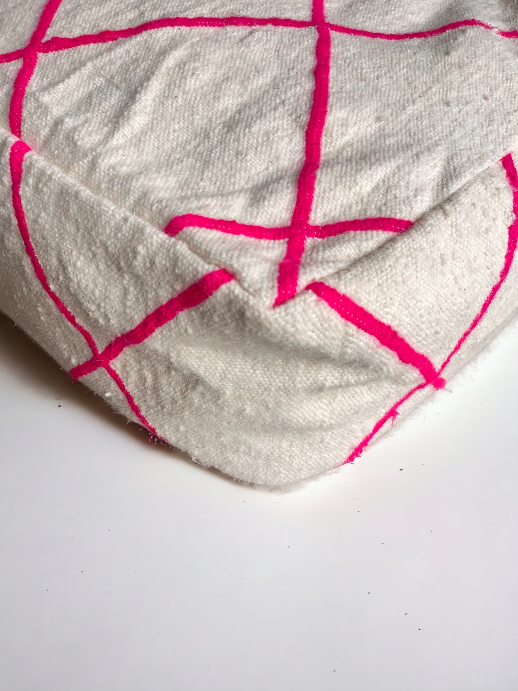 Eine Nahaufnahme des Bodenkissens - Mina von LEY! aus beigem Schurwolle-Stoff mit leuchtend rosa Gitterlinien auf weißem Untergrund - ideal als handgefertigtes Bodenkissen.