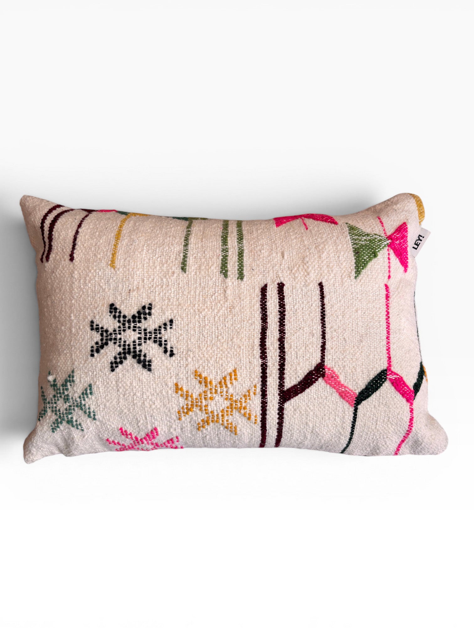 Das LEY! Kissen - Colorful Line - 40 x 60 von LEY! ist ein rechteckiges Kissen mit cremefarbenem Hintergrund, auf dem leuchtende geometrische Muster und Sterne in Pink, Gelb, Grün und Schwarz zu sehen sind. Hergestellt aus Schurwolle, inspiriert von Handarbeit Marrakesch.