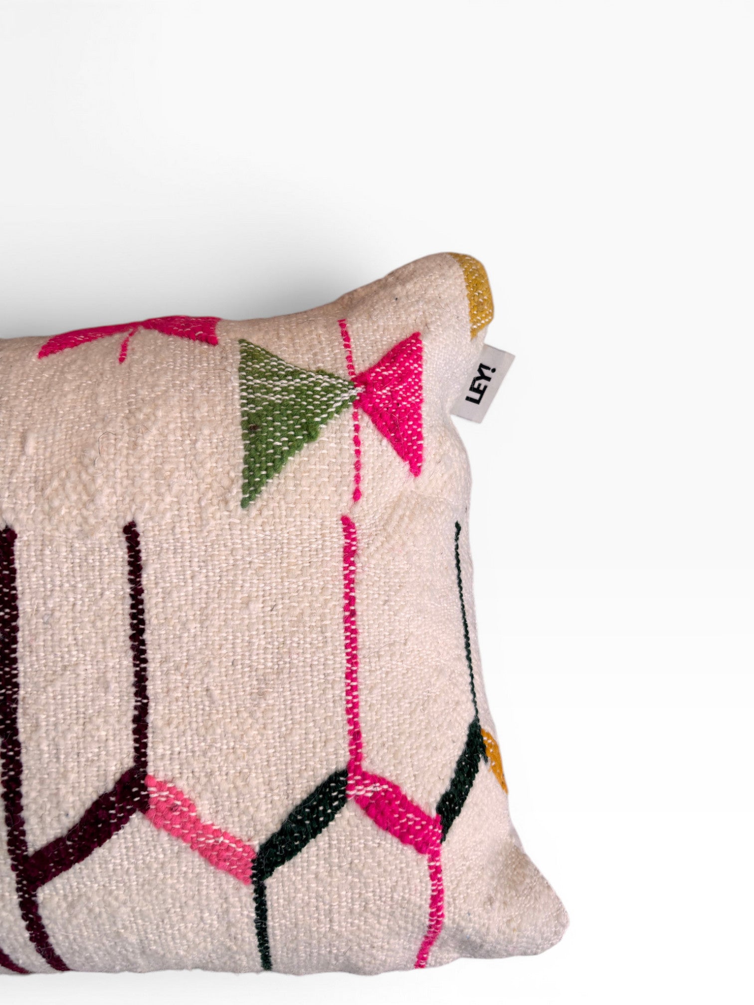 Das LEY! Kissen - Colorful Line - 40 x 60 von LEY! ist ein weißes, handgefertigtes Kissen aus Marrakeschwolle mit rosa, grünen, gelben und schwarzen geometrischen Linien und Dreiecken. In der Ecke befindet sich ein kleines "LEN"-Schild, das vor einem schlichten weißen Hintergrund steht.