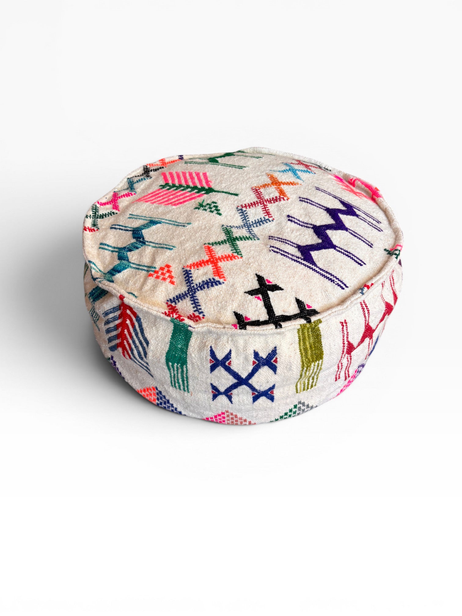 Das LEY! Bodenkissen - Colorful Line Round - Haraka ist ein beigefarbener Pouf mit lebendiger geometrischer und Zickzack-Stickerei in rosa, blauer, grüner, lila und orangefarbener Wolle - perfekt als Boho-Sitzkissen vor einem schlichten weißen Hintergrund.
