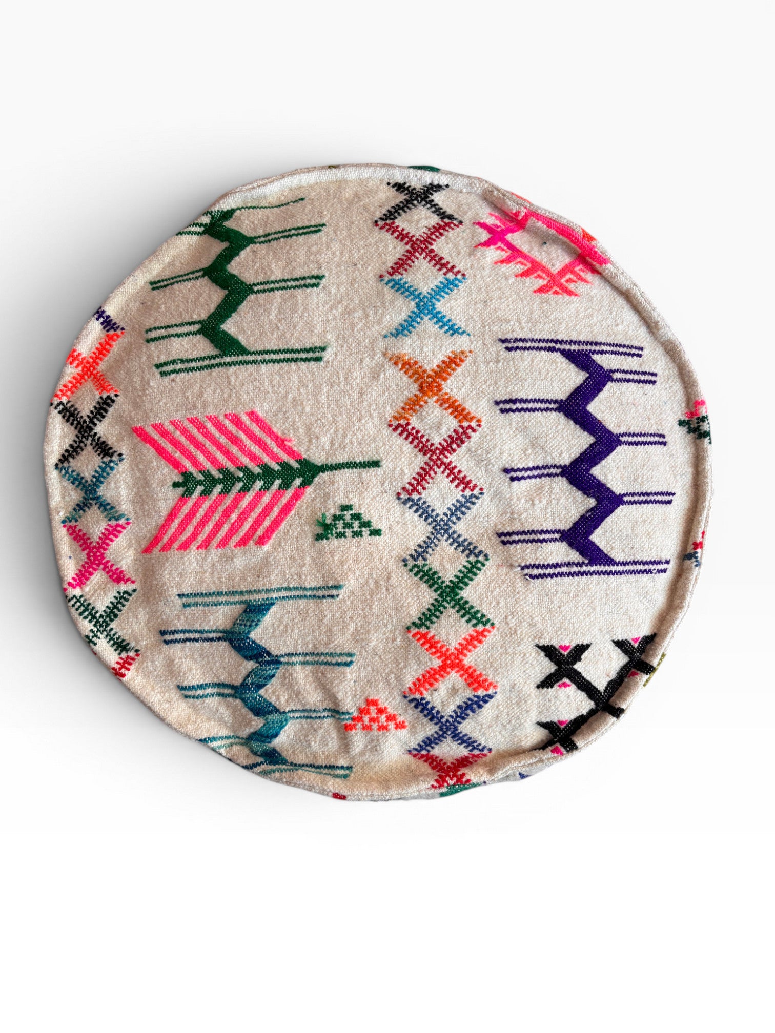 Das LEY! Bodenkissen - Colorful Line Round - Haraka ist ein rundes, beiges Boho-Bodenkissen mit lebhaften geometrischen und Zickzack-Mustern in Rosa, Grün, Blau, Orange, Lila und Schwarz auf weißem Hintergrund.