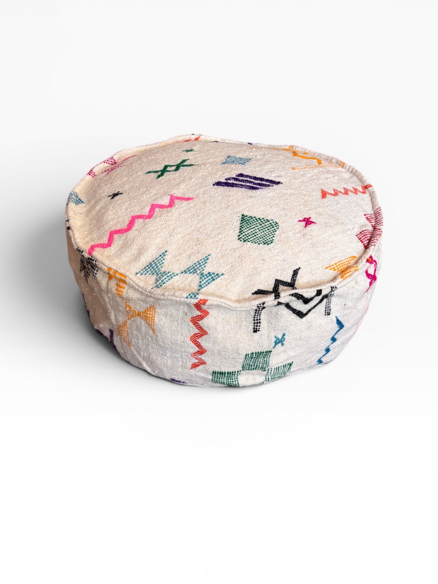Das LEY! Bodenkissen - Colorful Line Round - Tafika ist ein runder, cremefarbener Pouf mit bunten geometrischen und Zickzack-Mustern, gestickt auf weicher Schurwolle, abgebildet auf einem schlichten weißen Hintergrund.