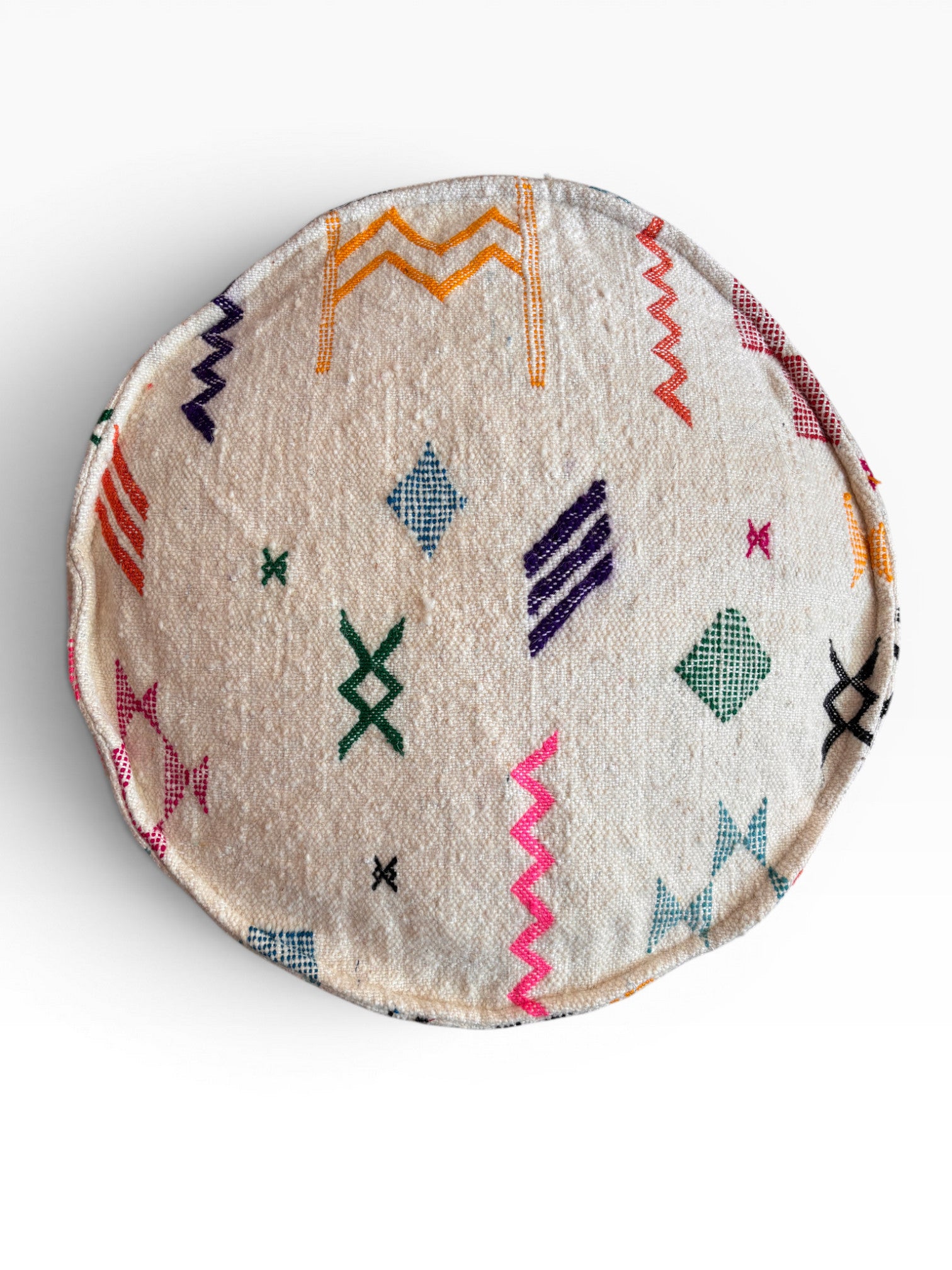 Das Bodenkissen - Colorful Line Round - Tafika von LEY! ist ein rundes, cremefarbenes Boho-Bodenkissen aus Schurwolle mit bunten geometrischen und Zickzack-Stickereien in Grün, Orange, Pink, Lila, Blau und Schwarz.