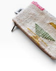 Die LEY! Tasche - Colorful Line - 15 x 20 hat ein strukturiertes Schurwolle-Design mit grünen, gelben und rosafarbenen gewebten Linien und einem weißen Etikett an der Oberseite. Diese multifunktionale Clutch steht auf einer schlichten weißen Oberfläche.
