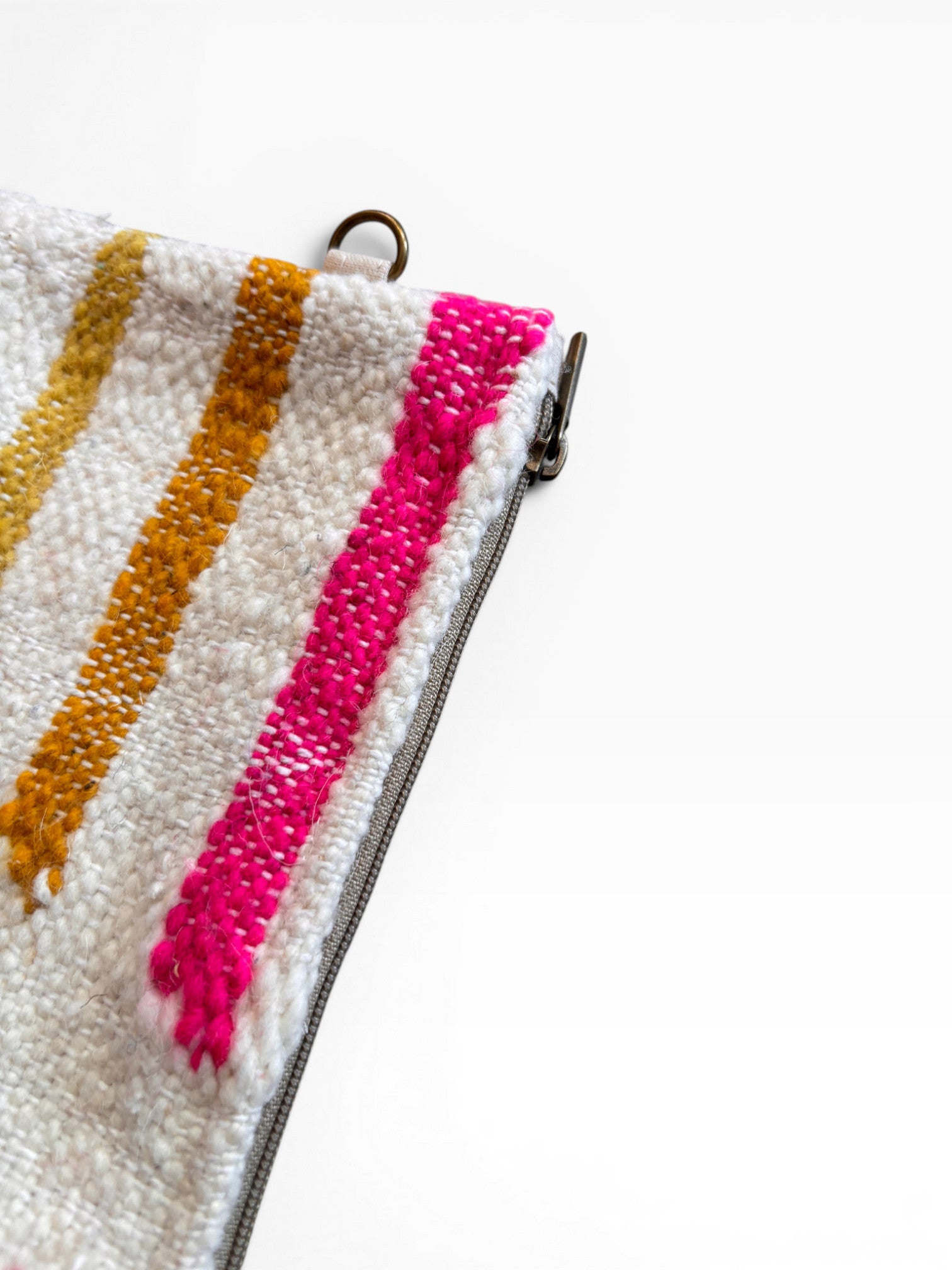 Nahaufnahme der Tasche - Colorful Line - 15 x 20 von LEY!: eine weiße, strukturierte Wolltasche mit gelben und rosafarbenen Diagonalstreifen, Metallreißverschluss und kleinem Metallring vor einem schlichten weißen Hintergrund.