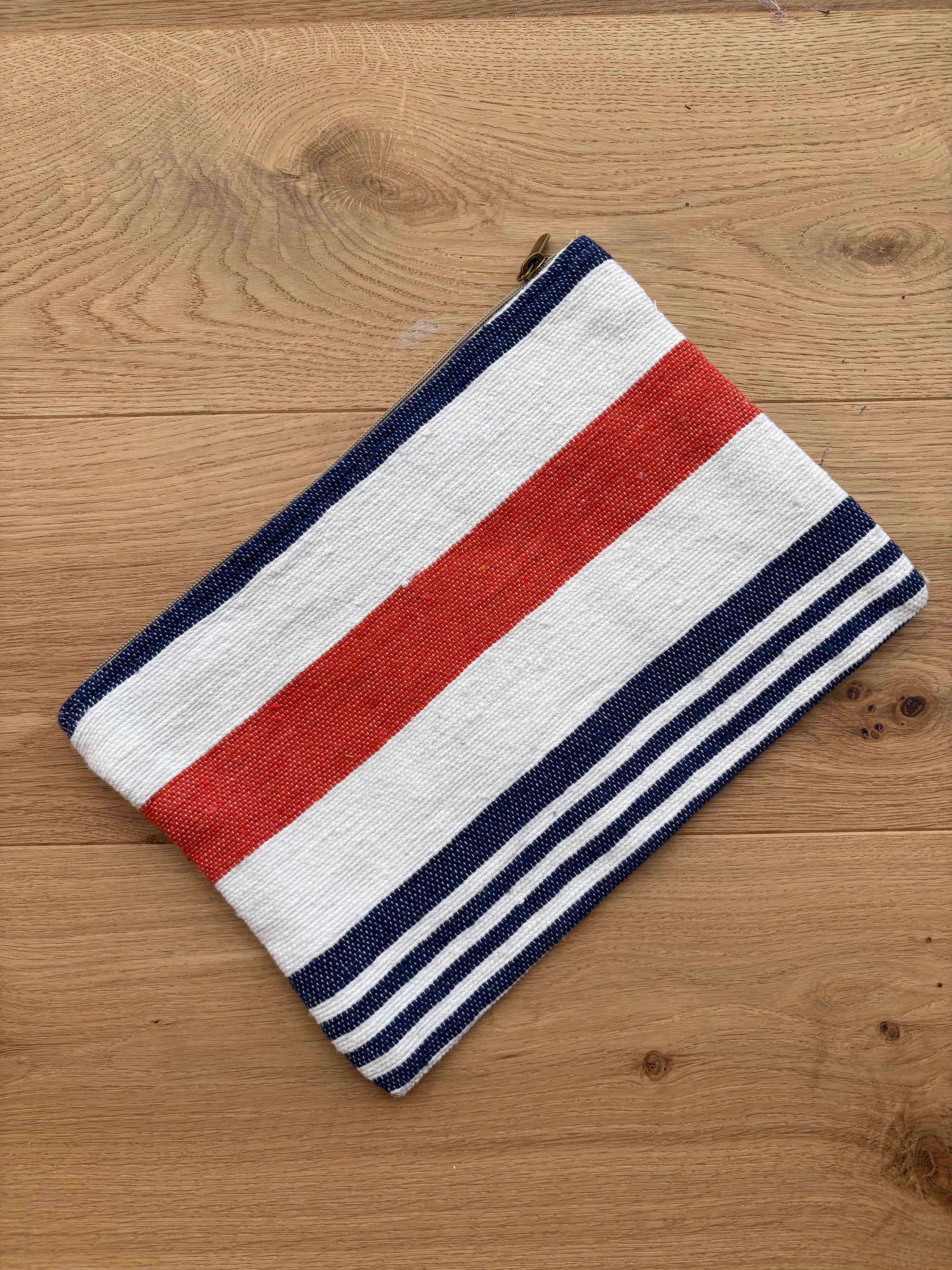 Die LEY! Tasche - Stripe Line "Parosa" (20x30cm) aus der Stripe Edition zeichnet sich durch kräftige und dünne Querstreifen in Rot, Weiß und Marineblau aus, die auf einer hellen Holzoberfläche abgebildet sind.