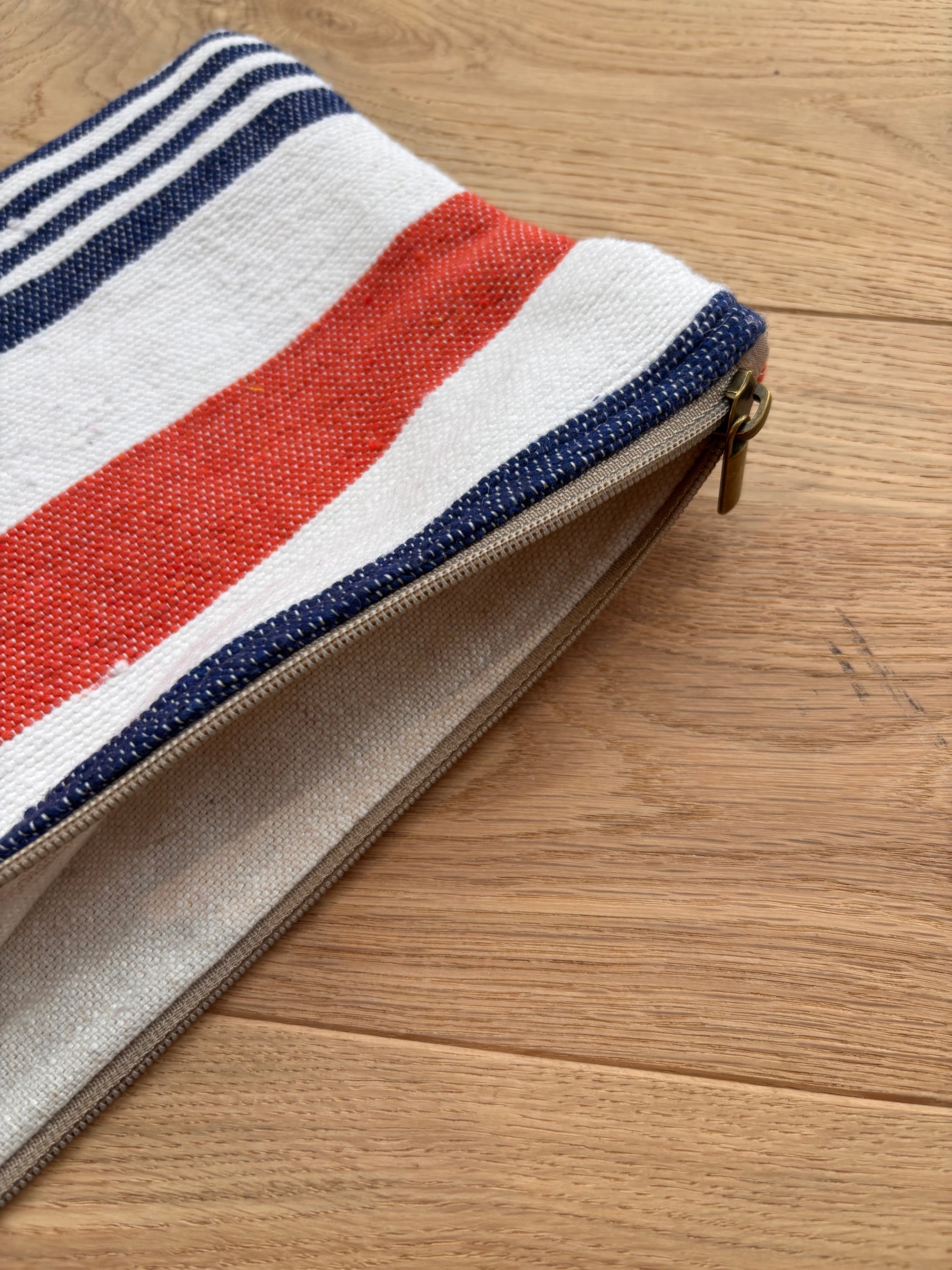 Die LEY! Tasche - Stripe Line "Parosa" (20x30cm), mit roten, weißen und blauen Streifen, liegt teilweise entpackt auf einer Holzunterlage.