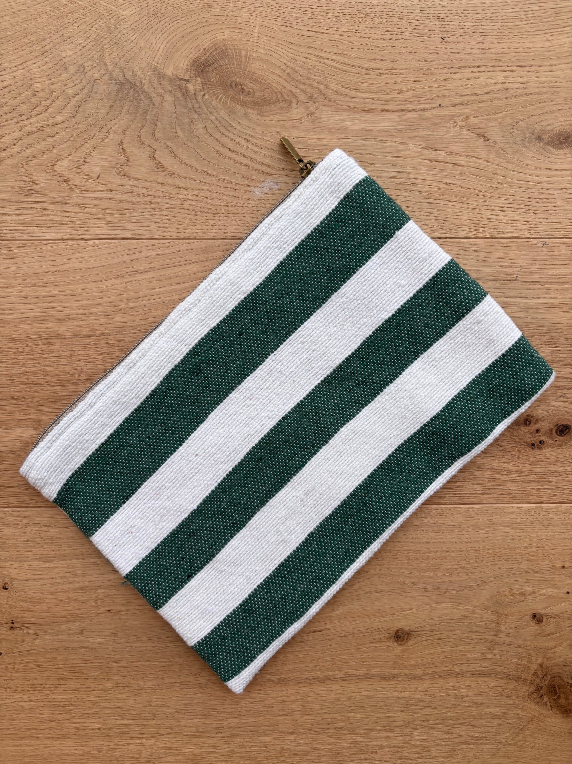 Die LEY! Tasche - Stripe Line "Tilosa" (20x30cm) ist eine handgefertigte Marrakesch-Baumwolltasche mit grünen und weißen Querstreifen und einem Reißverschluss, dargestellt auf einer hellen Holzoberfläche.