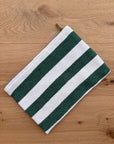 Die LEY! Tasche - Stripe Line "Tilosa" (20x30cm) ist eine handgefertigte Marrakesch-Baumwolltasche mit grünen und weißen Querstreifen und einem Reißverschluss, dargestellt auf einer hellen Holzoberfläche.