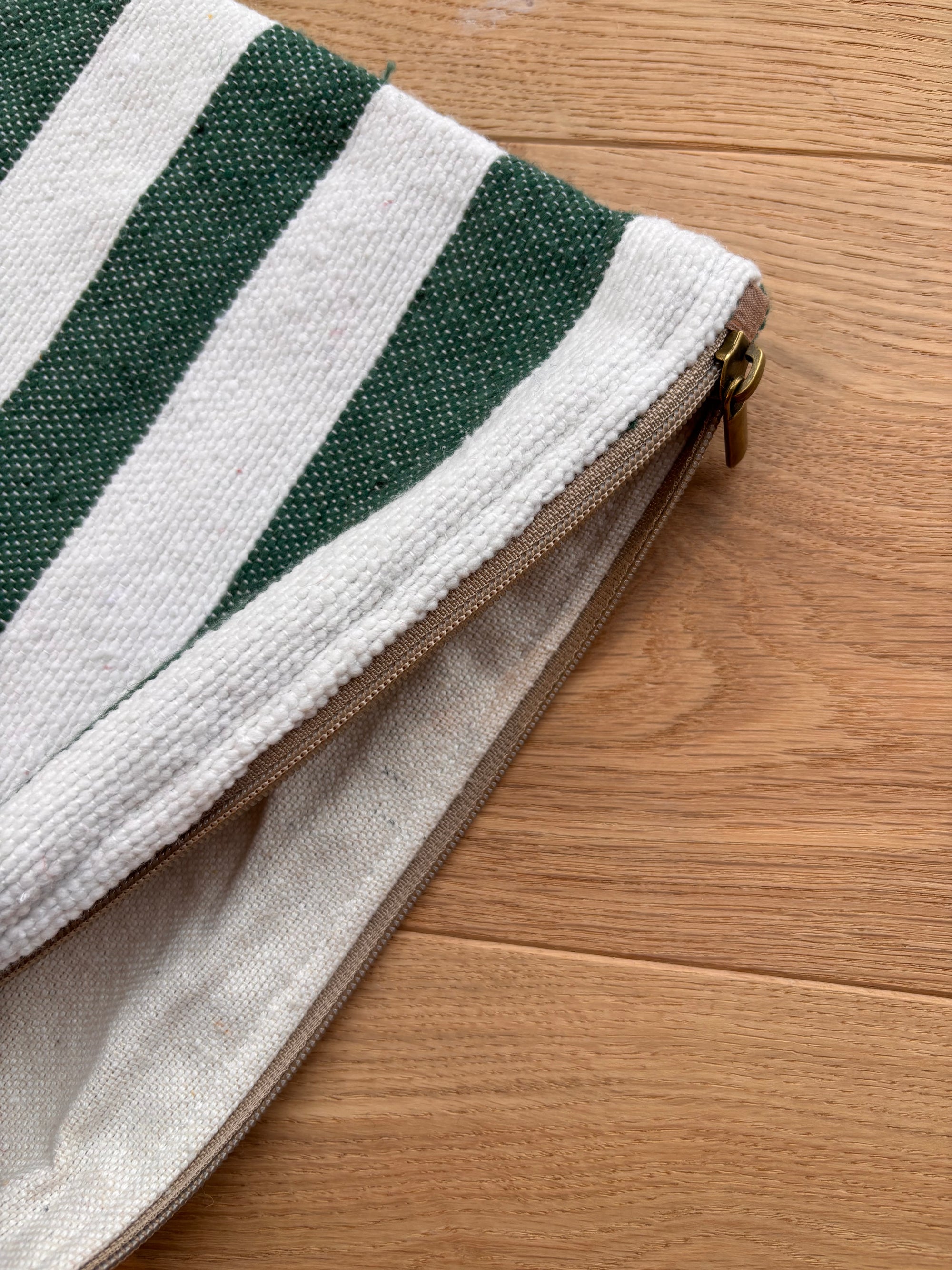 Eine Nahaufnahme der LEY! Tasche - Stripe Line "Tilosa" (20x30cm) mit grünen und weißen Streifen, teilweise entpackt, auf einer Holzunterlage liegend.