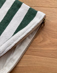 Eine Nahaufnahme der LEY! Tasche - Stripe Line "Tilosa" (20x30cm) mit grünen und weißen Streifen, teilweise entpackt, auf einer Holzunterlage liegend.