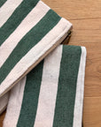 Zwei LEY! Tasche - Stripe Line "Tilosa" (20x30cm) mit grünen und cremefarbenen vertikalen Streifen und goldenen Reißverschlüssen sind überlappend auf Holz abgebildet.