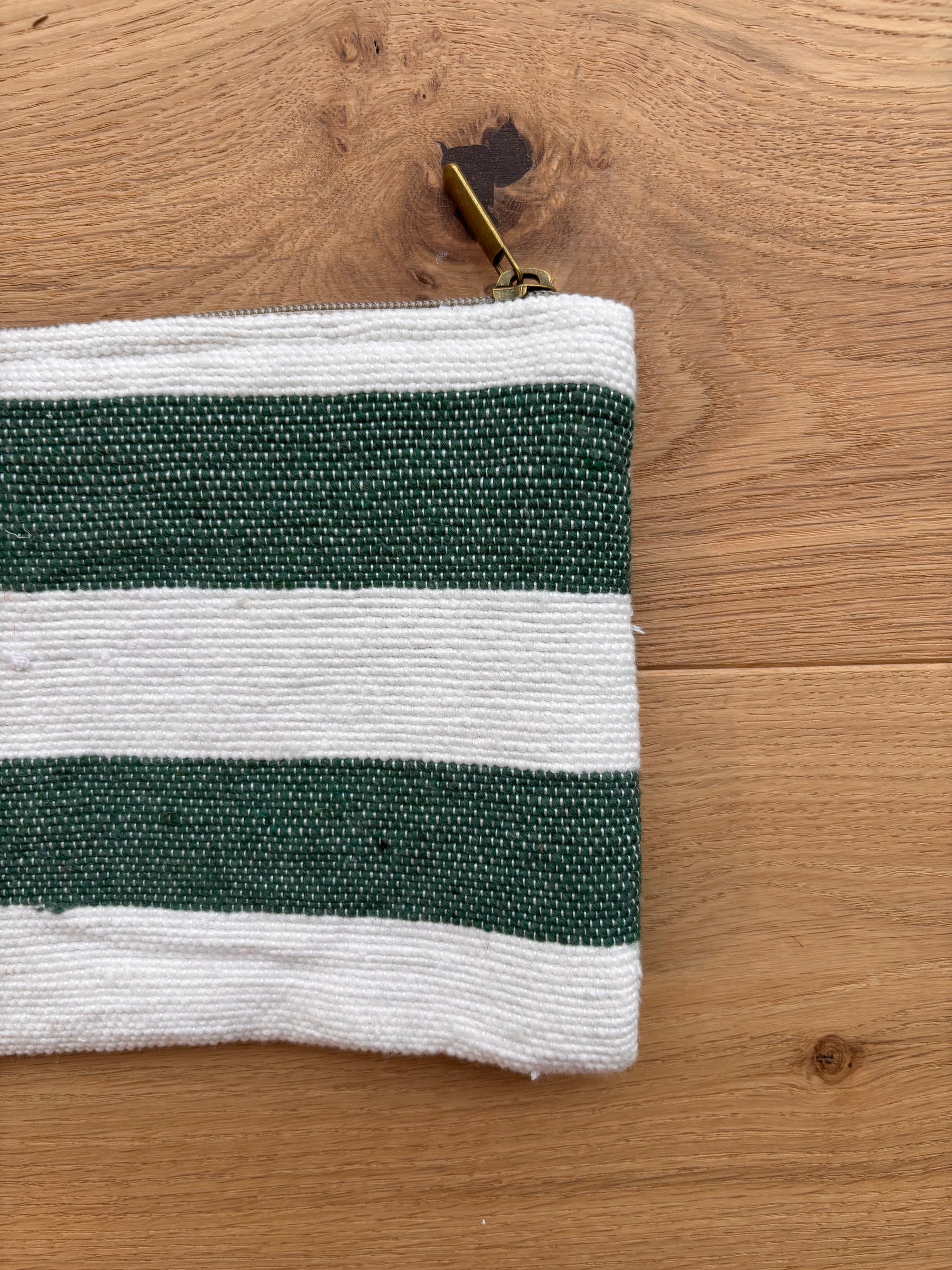 Eine grün-weiße LEY! Tasche - Stripe Line "Tilosa" (20x30cm) aus Baumwolle mit Messing-Reißverschluss liegt auf Holz, nur der obere linke Teil dieser handgefertigten Marrakesch-Tasche ist sichtbar.