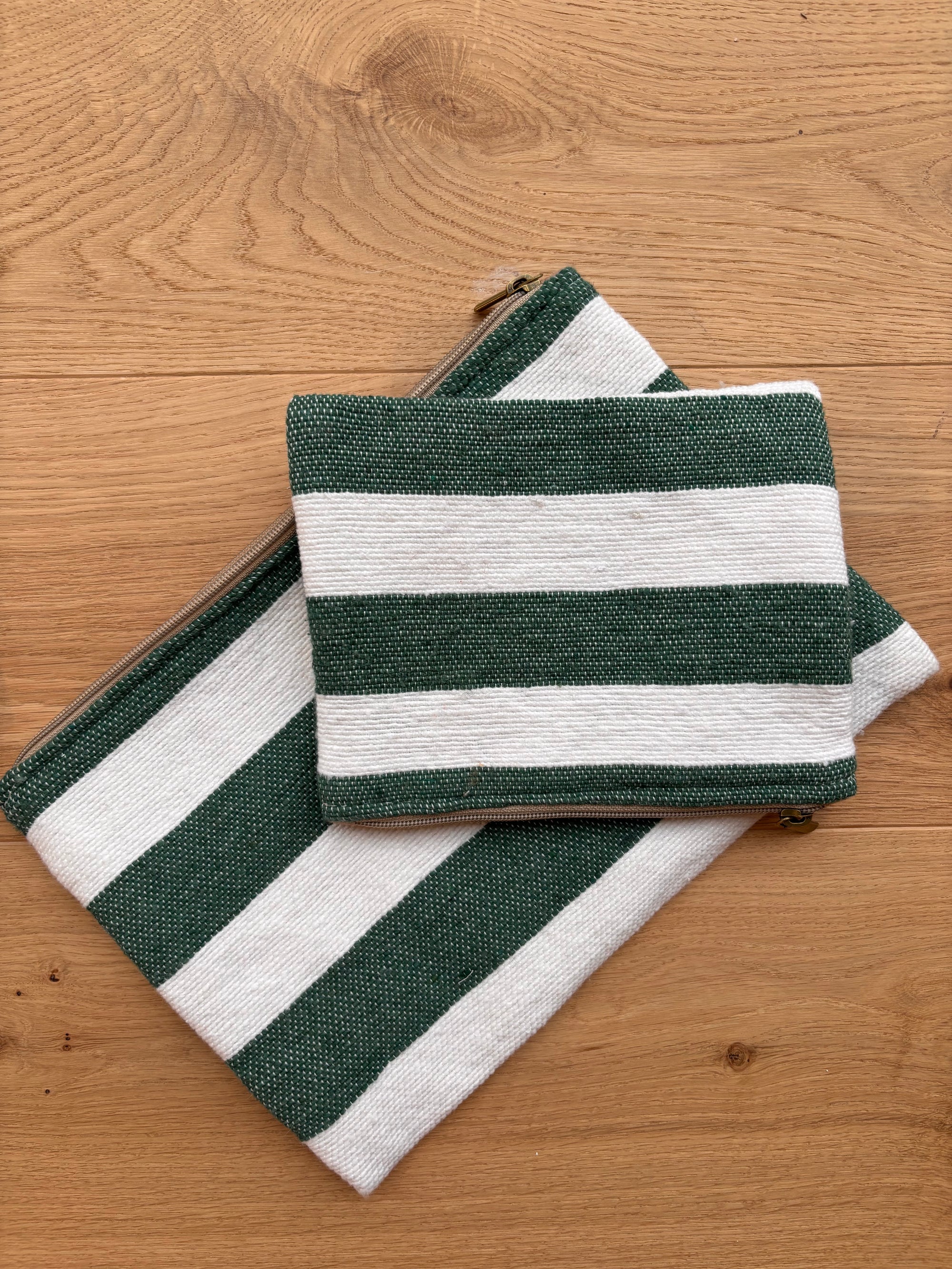 Zwei LEY! Tasche - Stripe Line "Tilosa" (20x30cm), handgefertigt mit grünen und weißen Streifen, eine kleine und eine große, beide mit Reißverschlüssen, abgebildet auf einer hellen Holzoberfläche.