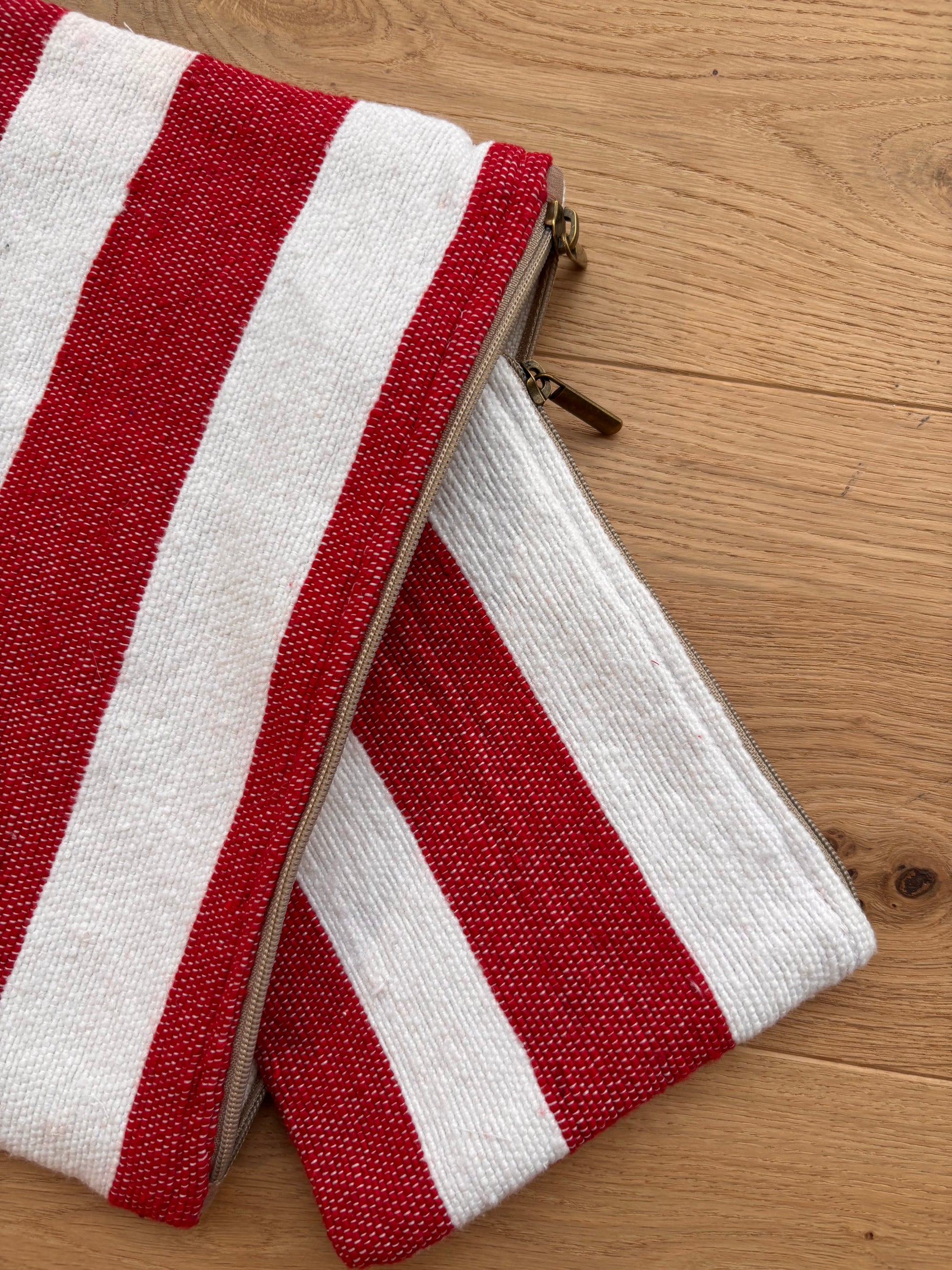 Zwei "Stripe Line 'Symia'" Taschen (20x30 cm) von LEY! im roten und weißen Streifendesign mit Zipper, leicht überlappend auf Holzfläche - stilvolle Handarbeit aus Marrakesch.