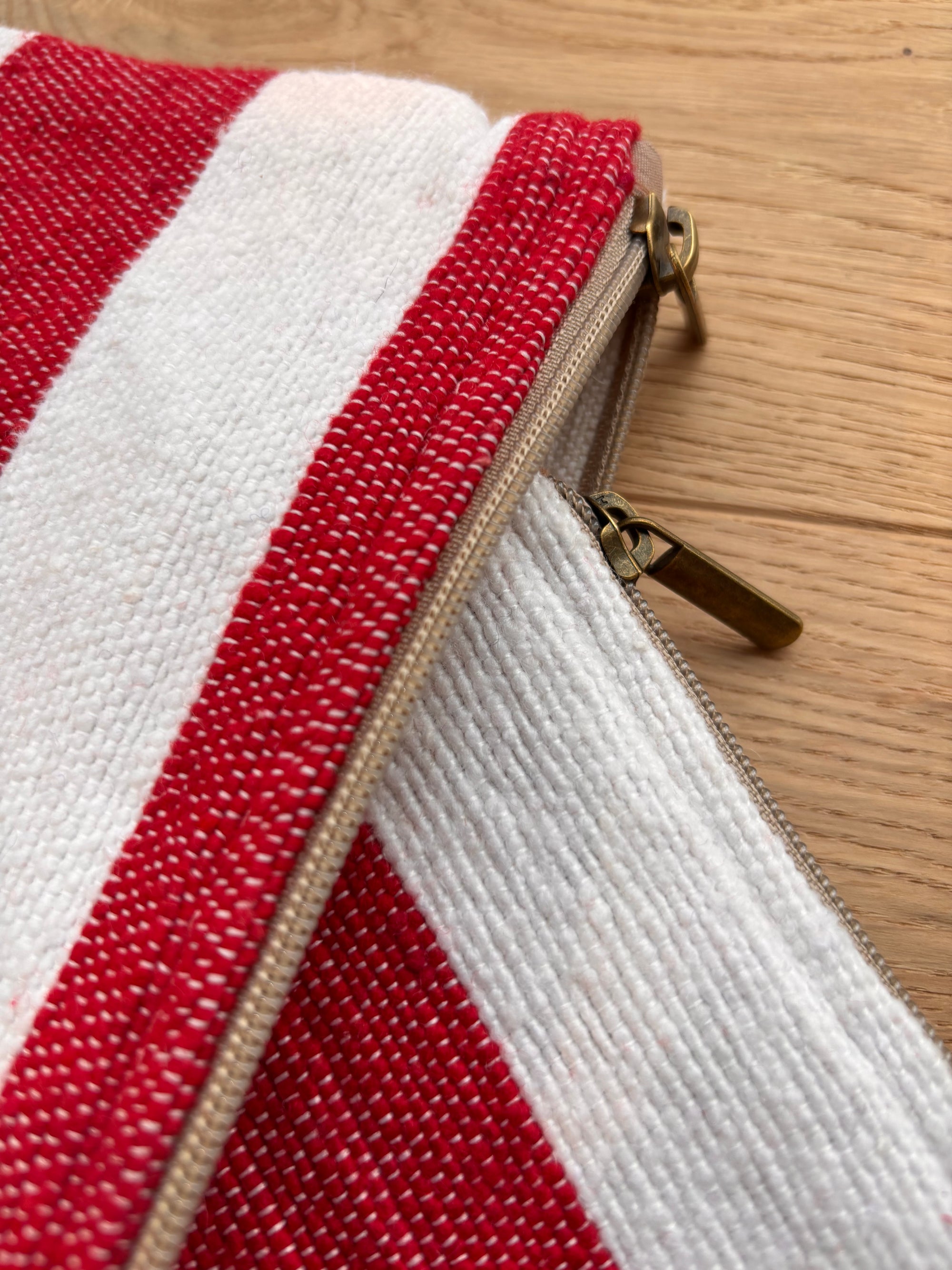Nahaufnahme der LEY! Tasche - Stripe Line "Symia" (20x30cm), handgefertigt in Marrakesch: rot-weißes Baumwoll-Streifendesign mit zwei tanfarbenen Zippern, liegend auf Holz.